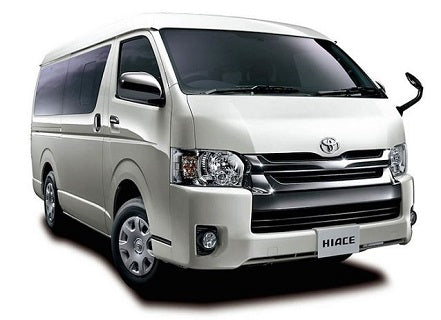 A group of five people standing in an airport terminal, likely at the arrival gate, with a man in a black suit and tie leading the group. Everyone is smiling and looking towards the camera.