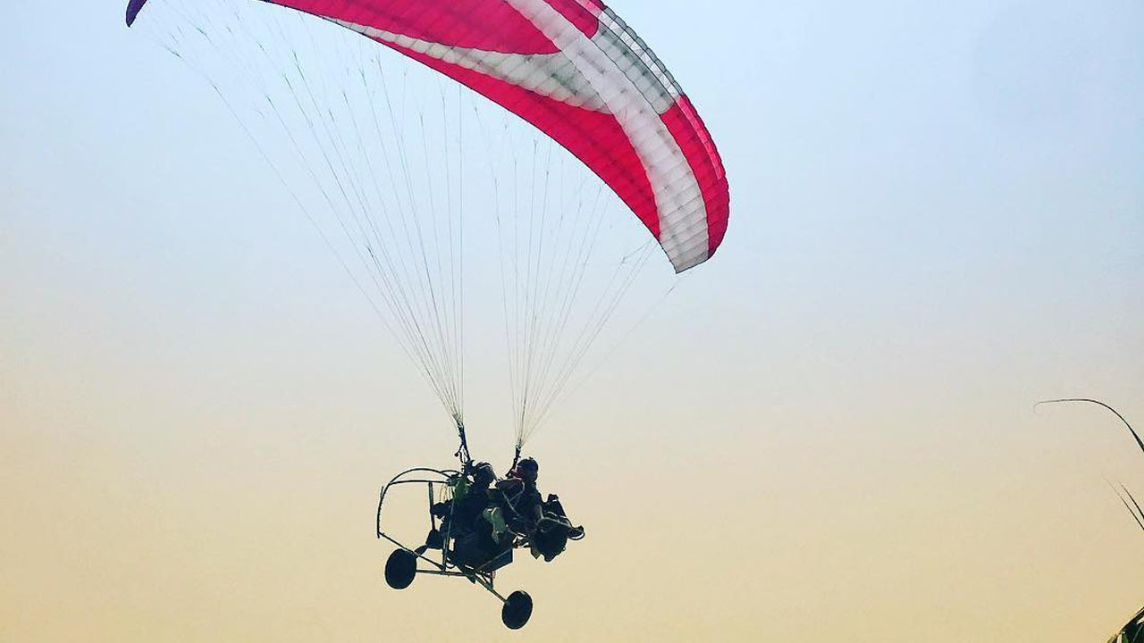 Person paragliding with a pink and white parachute against a clear sky.