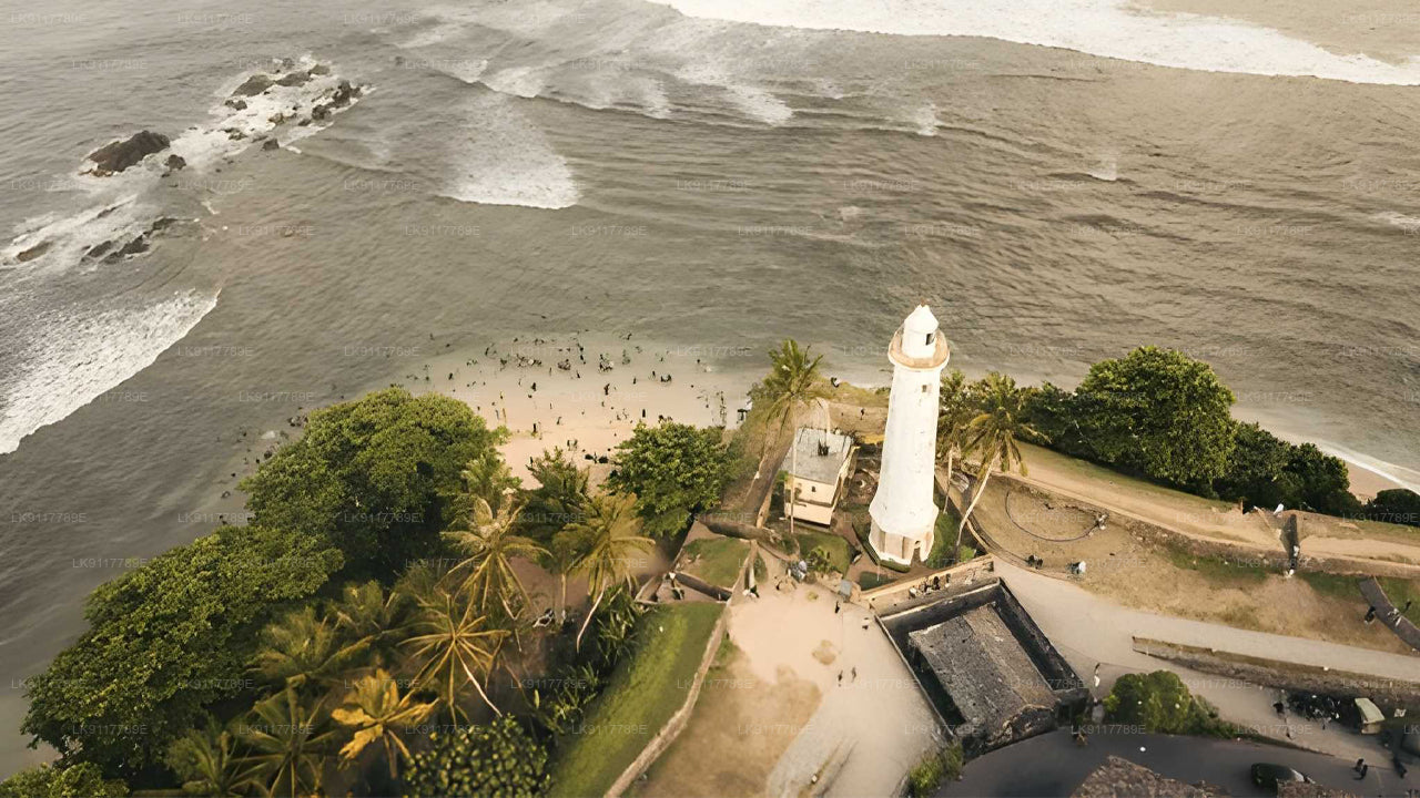 Lighthouse on a beach with trees and a fort-like structure nearby