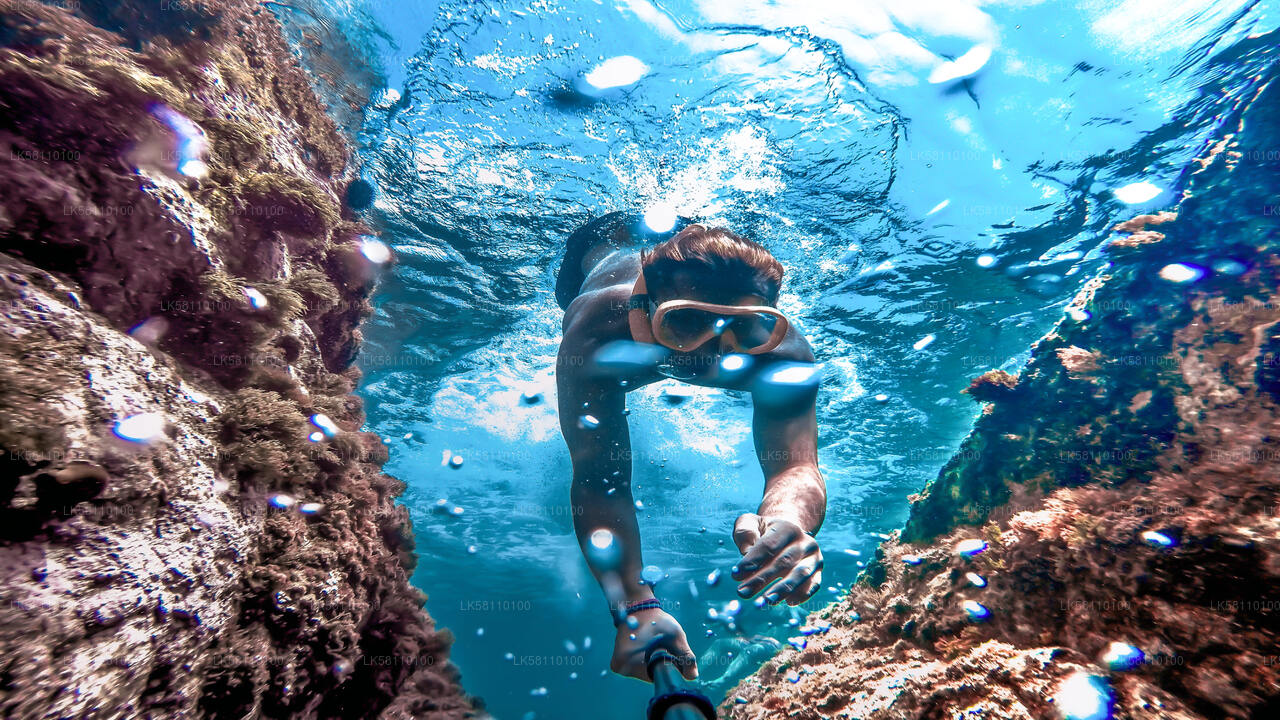Snorkeler swimming between coral rocks in clear blue Sri Lankan waters.